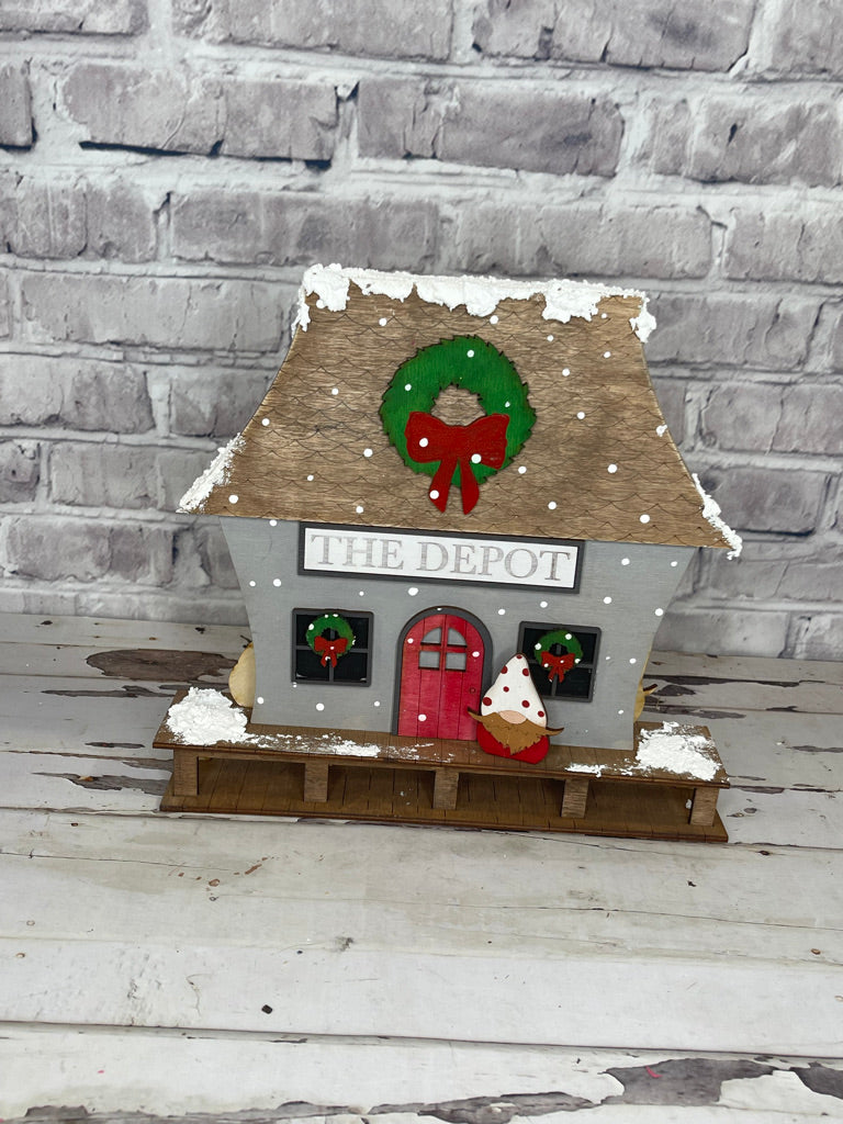 A small wooden house with Christmas Village Self Standing Double sided Pieces - TRAIN DEPOT - Winter Village Wood Blanks decorations on it from Little August Ranch.