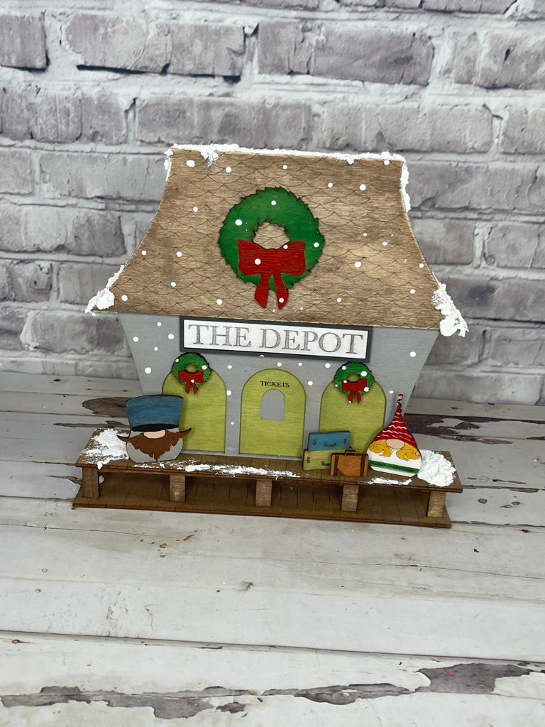 A wooden house with Little August Ranch Christmas Village Self Standing Double sided Pieces - TRAIN DEPOT - Winter Village Wood Blanks decorations on it.