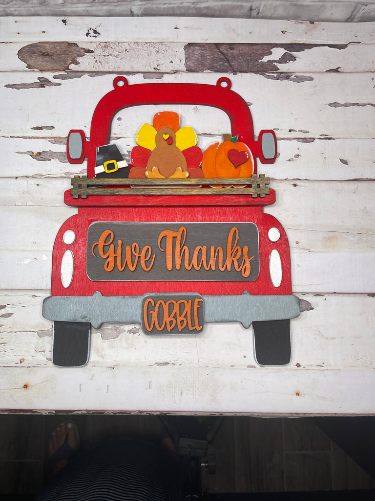 A red truck with turkeys and a thanksgiving sign, the Give Thanks Insert for Large Interchangeable Truck - Hanging or Self Standing Truck for Interchangeable Pieces from Little August Ranch, on a white wood surface.