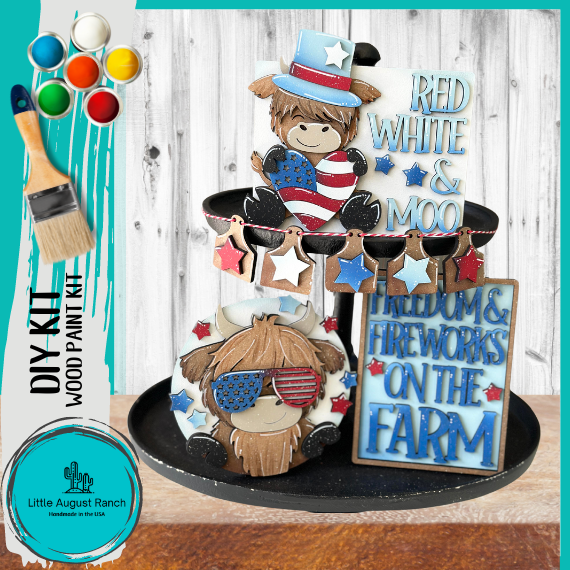A patriotic-themed DIY kit for a tiered tray display featuring painted wooden cutouts of a cow with American flag patterns, stars, and text that reads "red, white & moo" and "fre from Little August Ranch.