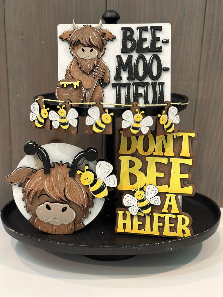 A tiered display featuring punny cow and bee-themed decorative signs with the phrases &quot;bee-moo-tiful&quot; and &quot;don&#39;t bee a heifer&quot; from our Little August Ranch Bee and Highland Cow Tiered Tray DIY Kit - Quick and Easy Tiered Tray Bundle.