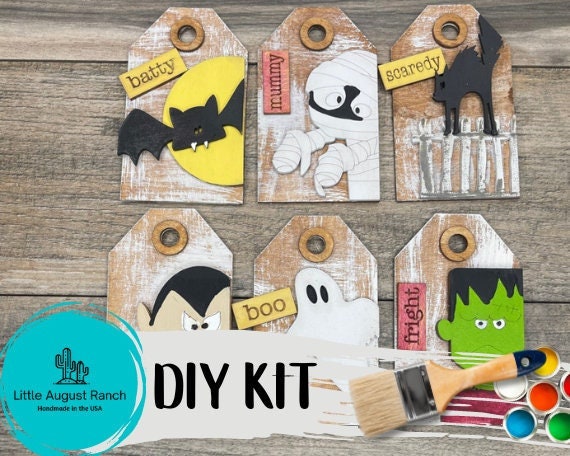 A DIY wood kit perfect for creating charming Tiered Tray Decor, featuring six Halloween-themed tags including a bat, mummy, black cat, vampire, ghost, and Frankenstein&#39;s monster. The Little August Ranch DIY Halloween Tags- Tree Ornament Wood Blanks i