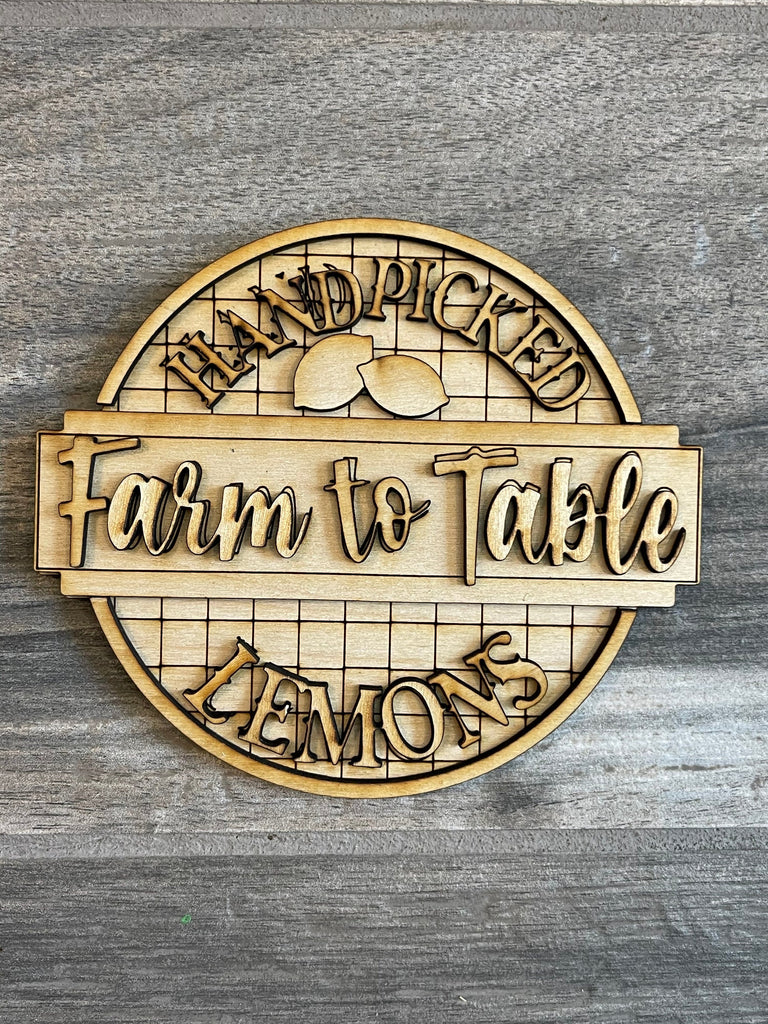 Circular wooden sign from the Lemon Tiered Tray DIY Paint Kit by Little August Ranch, with the text &quot;Hand Picked Farm to Table Lemons&quot; engraved, featuring a stylized lemon and leaf design, displayed on a gray wood background as part of a DIY Lemon Ti