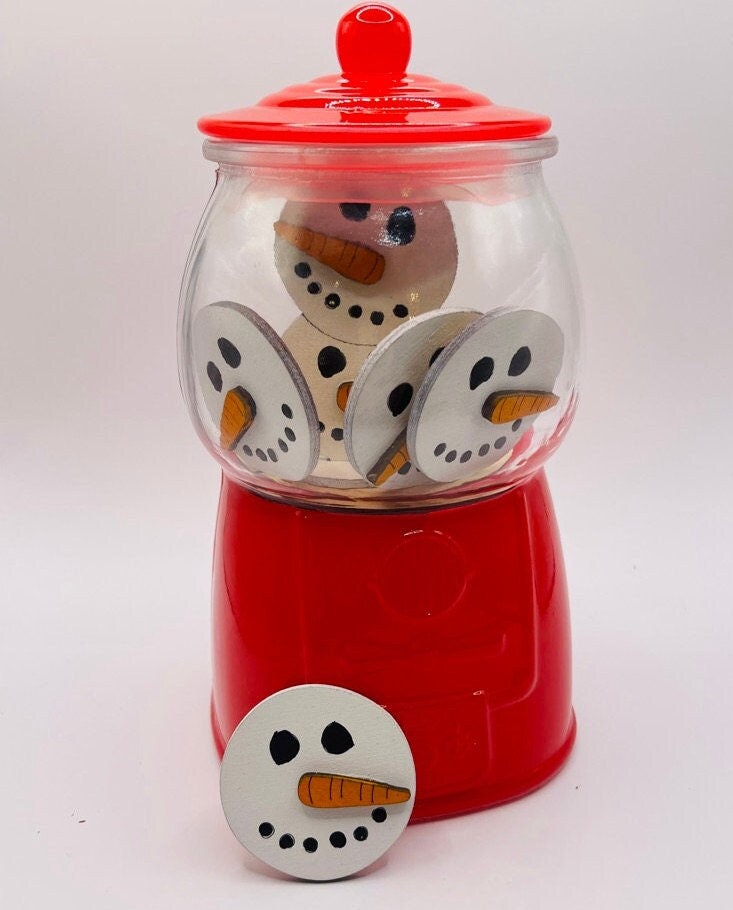 A red gum ball machine filled with wooden discs painted to look like snowman faces, including one disc placed outside on the base, makes a charming addition to any tiered tray. The Winter Gumball Machine Filler - DIY Gumball Filler Craft Kit by Littl