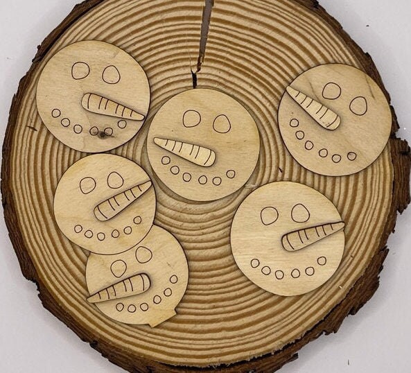 Five wooden discs with engraved snowman faces are arranged on a circular wooden surface with visible tree rings and a cracked center, perfect for adding to your Winter Gumball Machine Filler - DIY Gumball Filler Craft Kit by Little August Ranch or ti