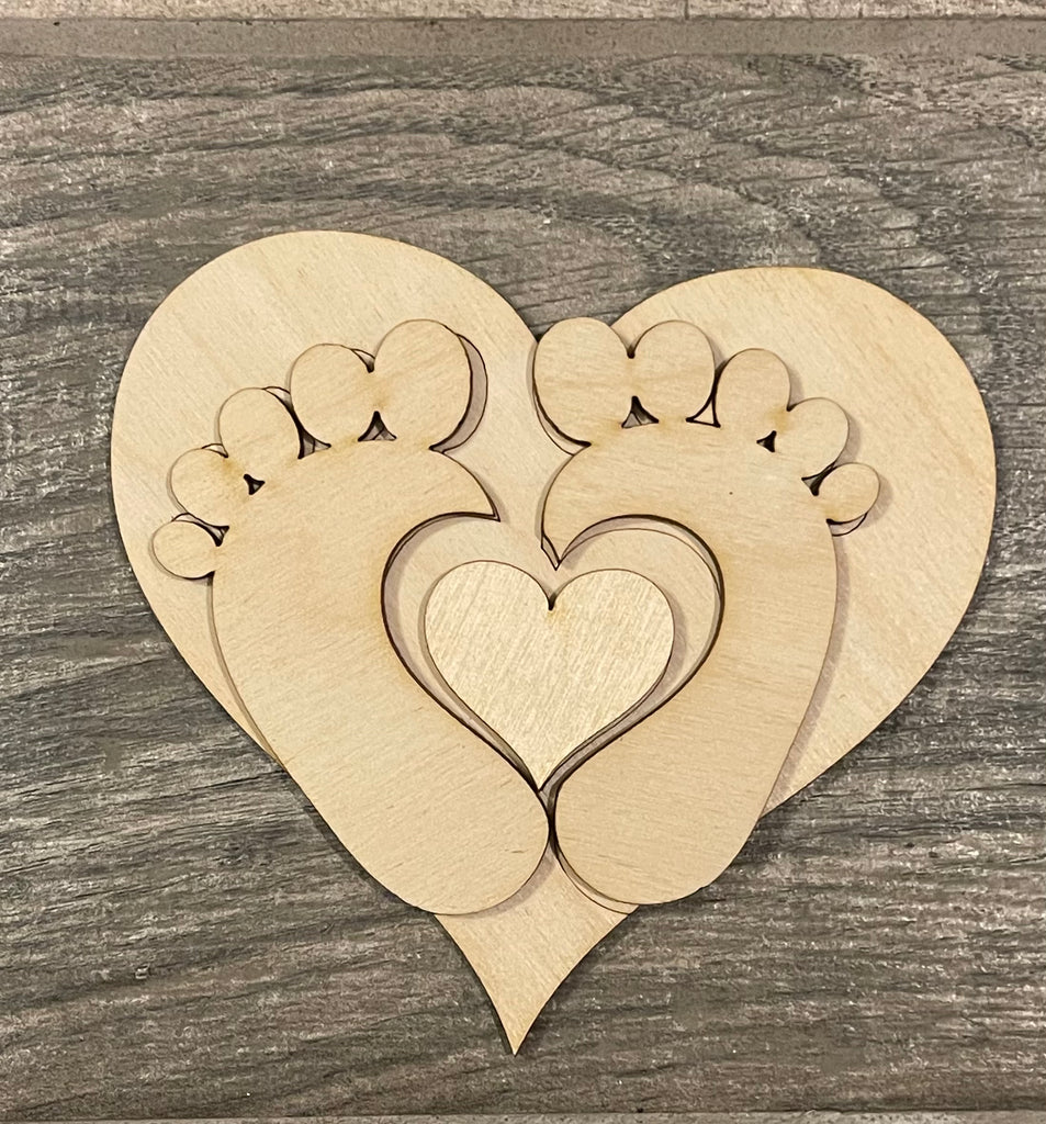 A wooden heart with a pair of baby feet on it, perfect for DIY paint and decorate projects or displaying on a Baby Tiered Tray DIY Kit - Baby Shower, Gender Reveal Wood Blanks from Little August Ranch with other wood items.