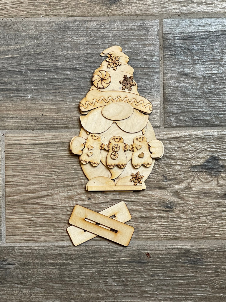 A wooden Gingerbread Gnome DIY - Standing Gnome on Base - Christmas DIY Paint Kit - DIY Shelf Decor ornament by Little August Ranch on a wooden floor.