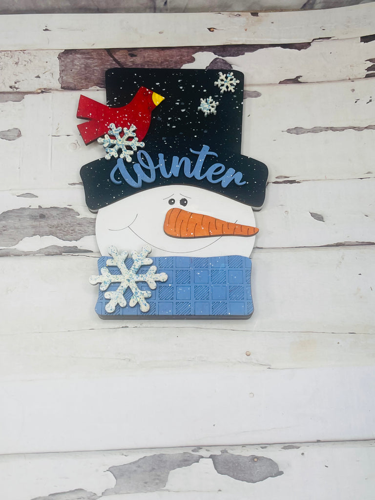 A Chunky Snowman Face DIY Paint Kit - Standing Decor Base - Winter Wood Blank - DIY Shelf Decor by Little August Ranch, and a cardinal hanging on a wooden wall.