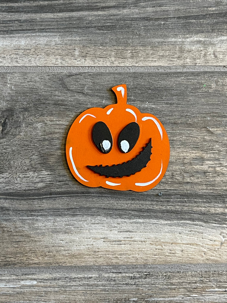 A large orange pumpkin with black eyes on a wooden surface, perfect for Halloween and Little August Ranch Halloween Tiered Tray Set - Finished Tiered Tray Bundle decor.