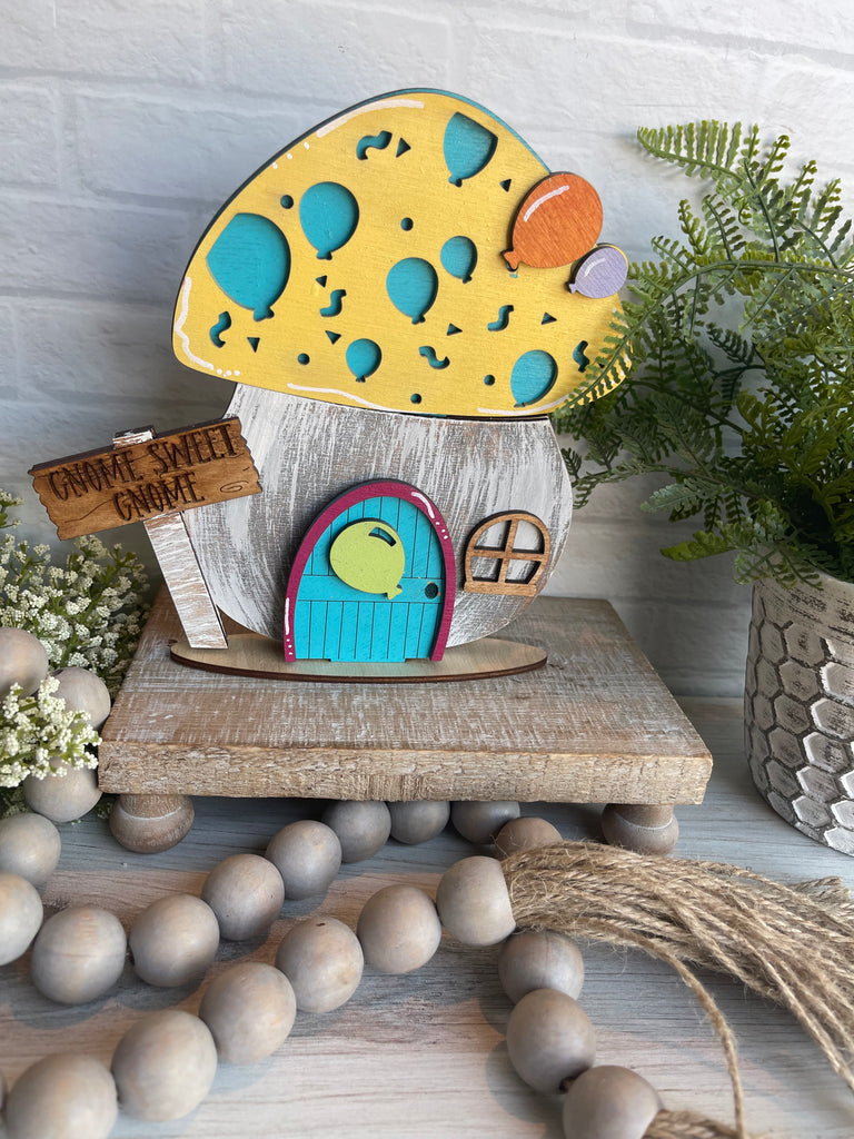 A Birthday Mushroom DIY Interchangeable Decor Inserts - Wood Paint Kit - Insert, resembling a wooden mushroom house, rests atop a quaint wooden table at Little August Ranch.