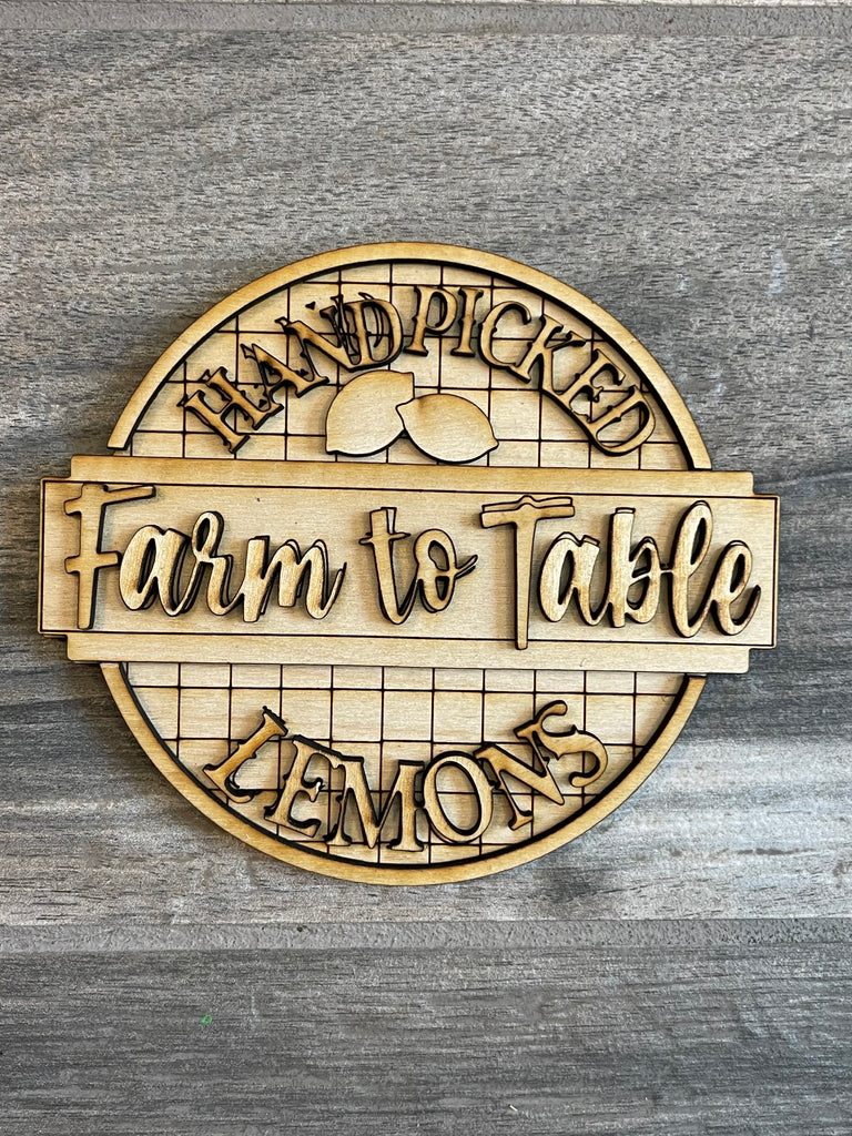 Circular wooden sign from the Lemon Tiered Tray DIY Paint Kit by Little August Ranch, with the text "Hand Picked Farm to Table Lemons" engraved, featuring a stylized lemon and leaf design, displayed on a gray wood background as part of a DIY Lemon Tiered Tray Kit.