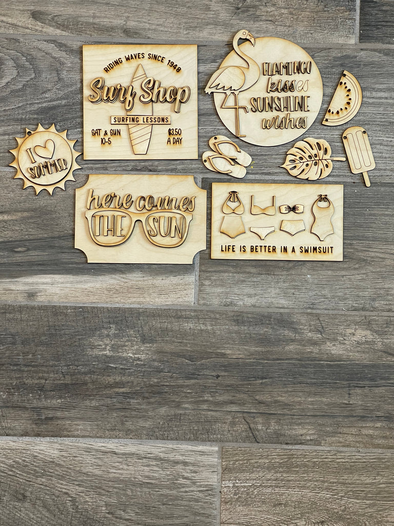 A collection of wooden DIY Summer Beach Tiered Tray - Surf Shop Tier Tray Bundle decorative signs and symbols, including a Little August Ranch paint kit, arranged on a tiered tray on a wooden floor.