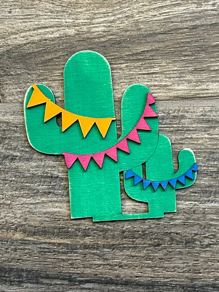A green cactus with colorful bunting on a wooden surface for a DIY Mexican Fiesta featuring Fiesta Freestanding Wood Gnome Outfits- Cinco de Mayo Interchangeable Gnomes from Little August Ranch.