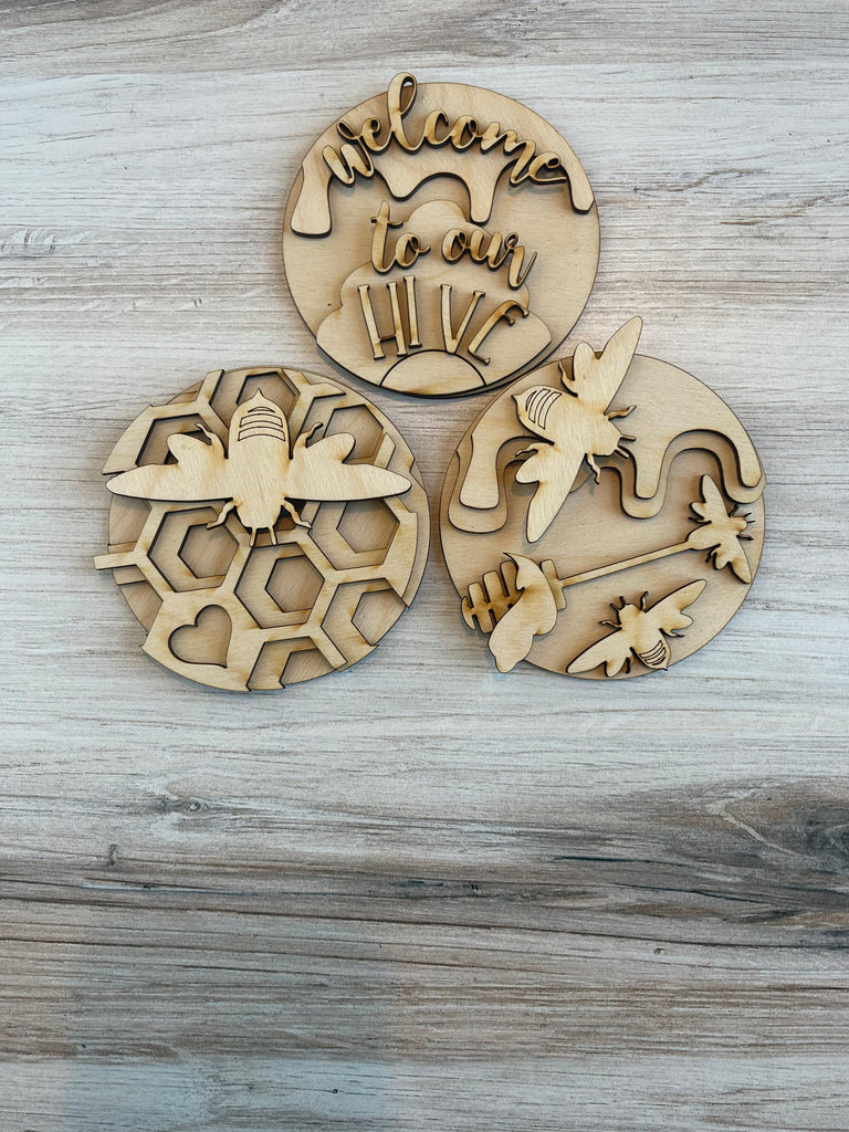 Three interchangeable wooden coasters adorned with honey bee designs from Little August Ranch's Bee Circle Trio DIY Wood Paint Kit for 3 Circle Frame - Interchangeable Decor.